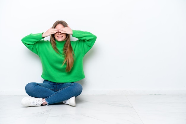 Young caucasian woman sitting on the floor isolated on white background covering eyes by hands