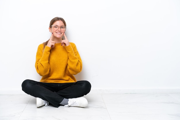 Young caucasian woman sitting on the floor isolated on white background smiling with a happy and pleasant expression