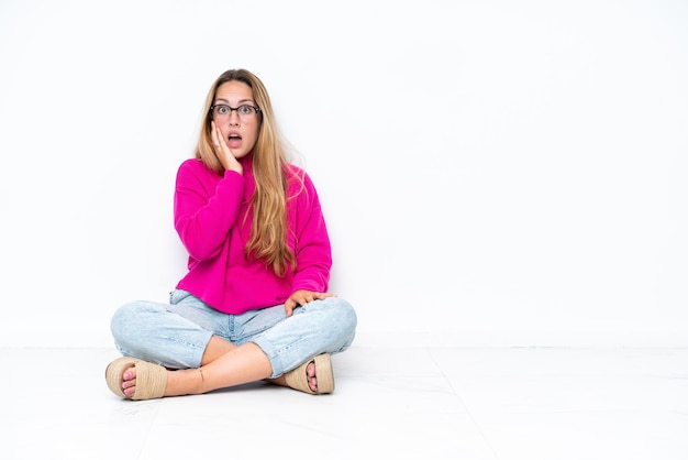 Young caucasian woman sitting on the floor isolated on white background surprised and shocked while looking right