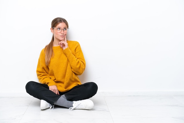 Young caucasian woman sitting on the floor isolated on white background thinking an idea while looking up