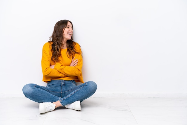 Young caucasian woman sitting on the floor isolated on white wall happy and smiling