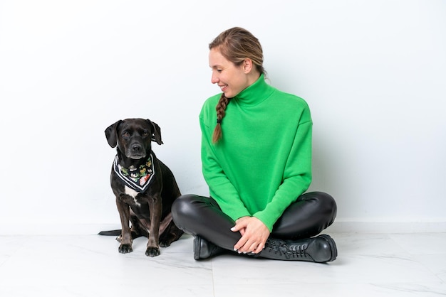 Young caucasian woman sitting on the floor with his puppy isolated on white background with happy expression