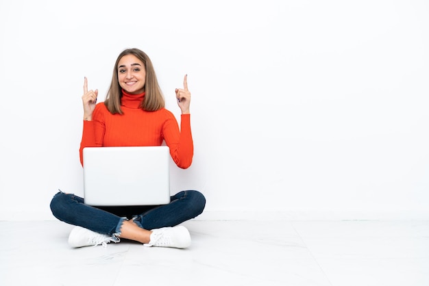 Young caucasian woman sitting on the floor with a laptop pointing up a great idea