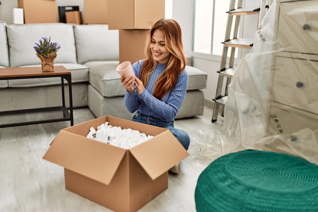 Young caucasian woman smiling confident unpacking cardboard box at new home