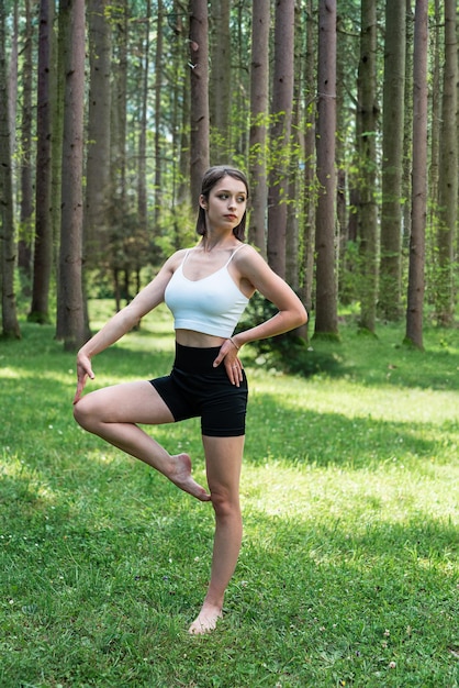 Young caucasian woman in sportwear practicing yoga on green grass in the park