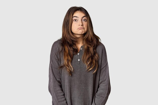 Photo young caucasian woman in studio setting shrugs shoulders and open eyes confused