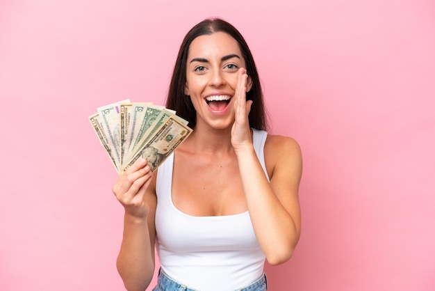 Young caucasian woman taking a lot of money isolated on pink background shouting with mouth wide open