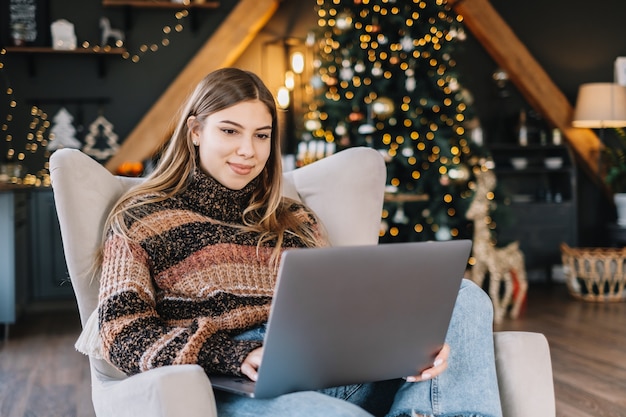 Young caucasian woman using laptop computer in holidays at home in the armchair in living room.