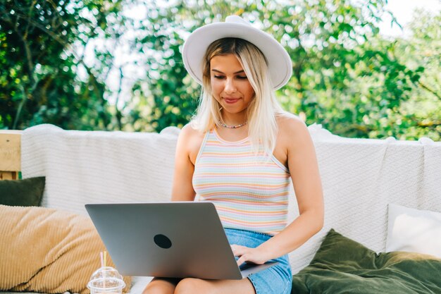 Young caucasian woman using laptop computer outdoor, sitting on a bench in the backyard in summer day.