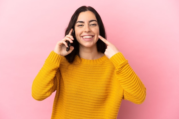 Young caucasian woman using mobile phone isolated on pink background giving a thumbs up gesture