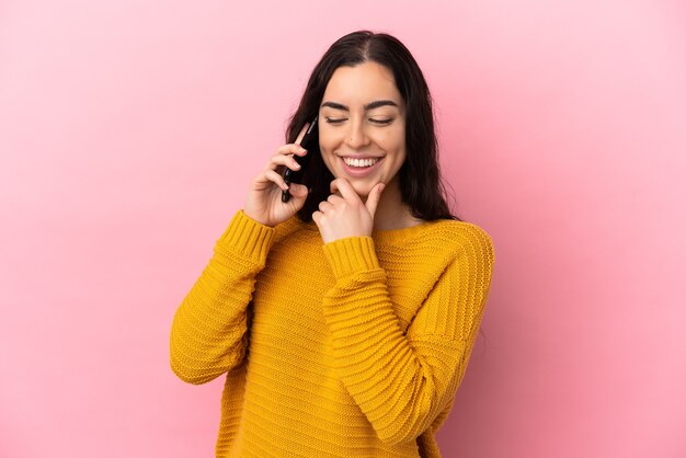 Young caucasian woman using mobile phone isolated on pink background looking to the side and smiling