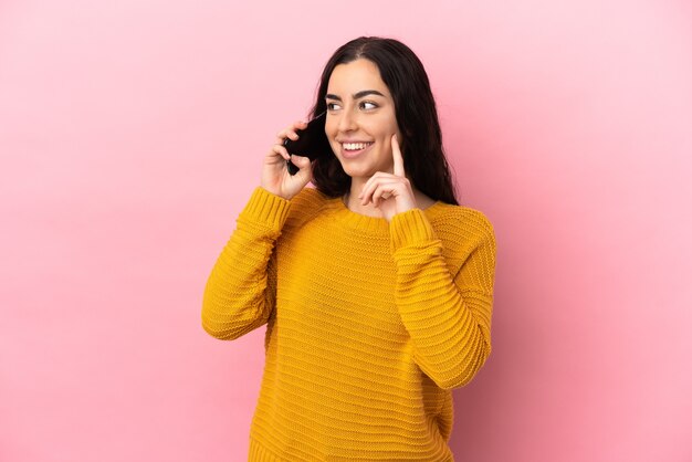 Young caucasian woman using mobile phone isolated on pink background thinking an idea while looking up