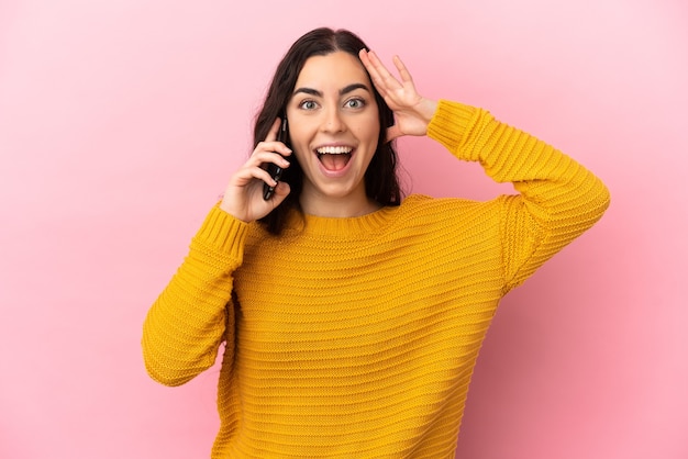 Young caucasian woman using mobile phone isolated on pink background with surprise expression