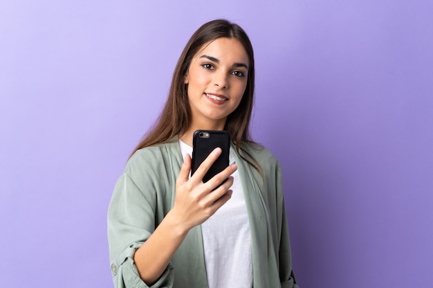 Young caucasian woman using mobile phone isolated on purple wall with happy expression