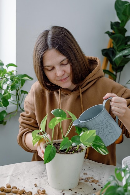 A young caucasian woman watering just potted scindapsus epipremnum houseplant