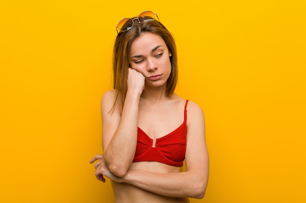 Young caucasian woman wearing bikini and sunglasses who feels sad and pensive, looking at copy space.