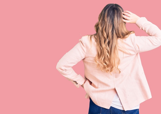 Young caucasian woman wearing business clothes backwards thinking about doubt with hand on head