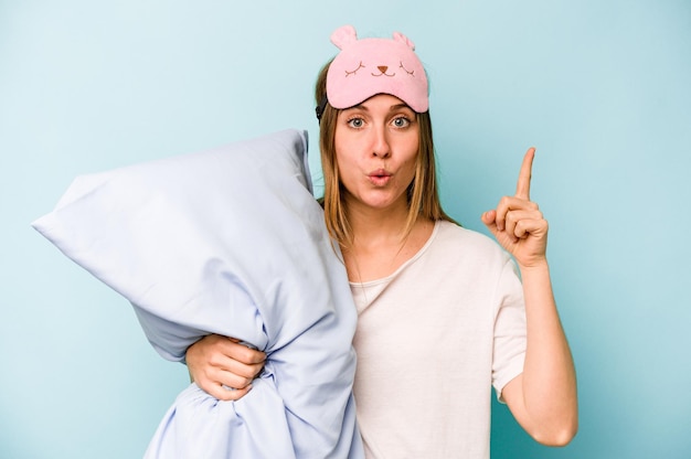 Young caucasian woman wearing a pajama isolated on blue background having some great idea concept of creativity