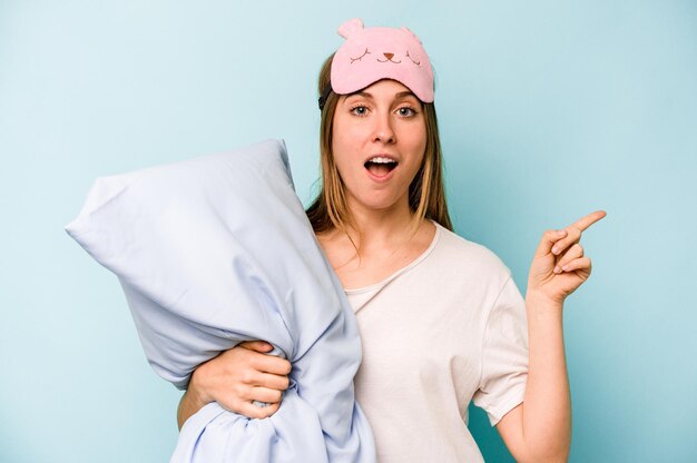 Young caucasian woman wearing a pajama isolated on blue background pointing to the side