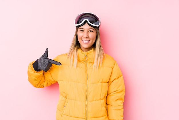 Young caucasian woman wearing a ski clothes in a pink background person pointing by hand to a shirt copy space, proud and confident