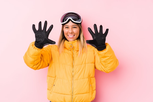 Young caucasian woman wearing a ski clothes in a pink wall showing number ten with hands.