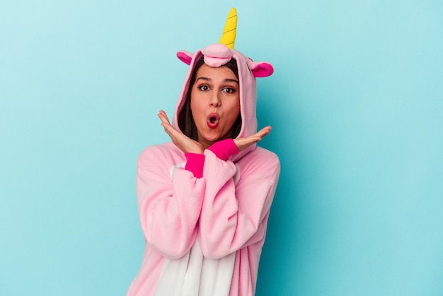 Young caucasian woman wearing an unicorn pajama isolated on blue background