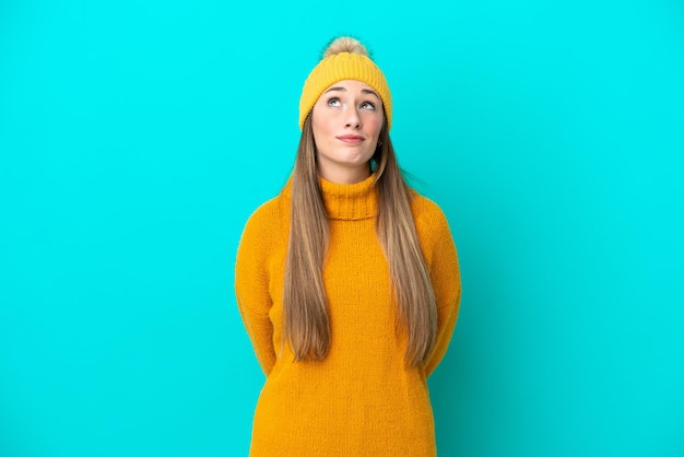 Photo young caucasian woman wearing winter jacket isolated on blue background and looking up