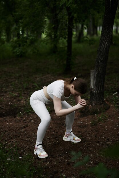 Photo young caucasian woman in white sportswear exercising in green forest park