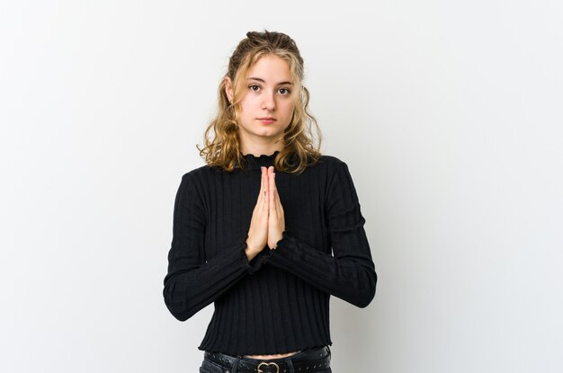 Photo young caucasian woman on white wall praying, showing devotion