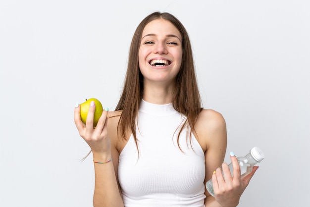 Young caucasian woman on white wall with an apple and with a bottle of water