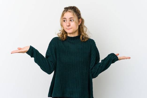 Young caucasian woman on white wallconfused and doubtful shrugging shoulders to hold a copy space.