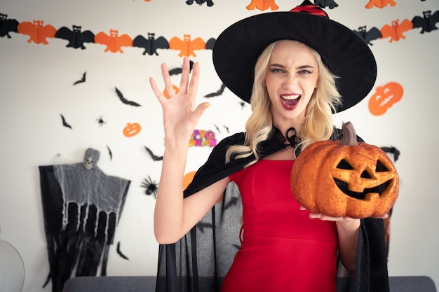 Young caucasian woman in witch clothing holding pumpkin party at home