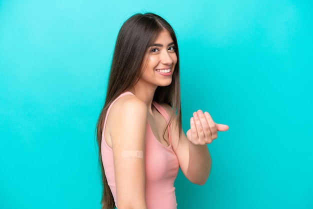 Young caucasian woman with band aids isolated on blue background inviting to come with hand Happy that you came