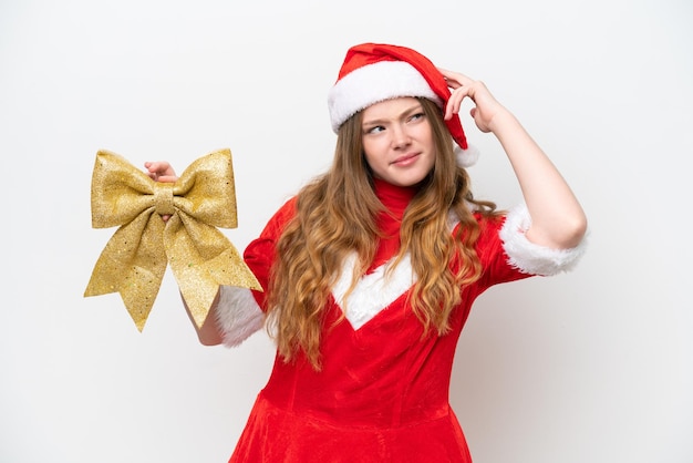 Young caucasian woman with Christmas dress holding Christmas bow isolated on white background having doubts and with confuse face expression