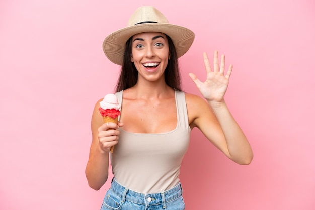 Young caucasian woman with a cornet ice cream isolated on pink background counting five with fingers