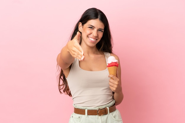 Young caucasian woman with a cornet ice cream isolated on pink background shaking hands for closing a good deal