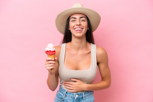 Young caucasian woman with a cornet ice cream isolated on pink background smiling a lot