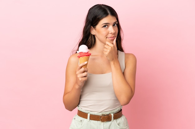 Young caucasian woman with a cornet ice cream isolated on pink background thinking