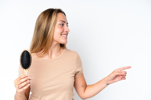 Photo young caucasian woman with hair comb isolated on white background pointing to the side to present a product