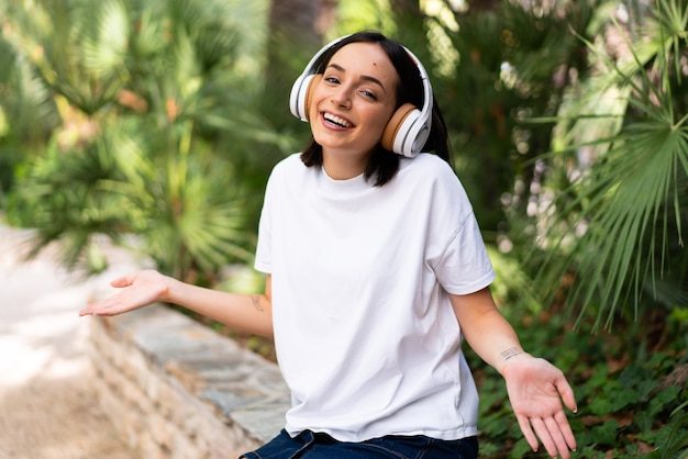 Young caucasian woman with headphones at outdoors smiling