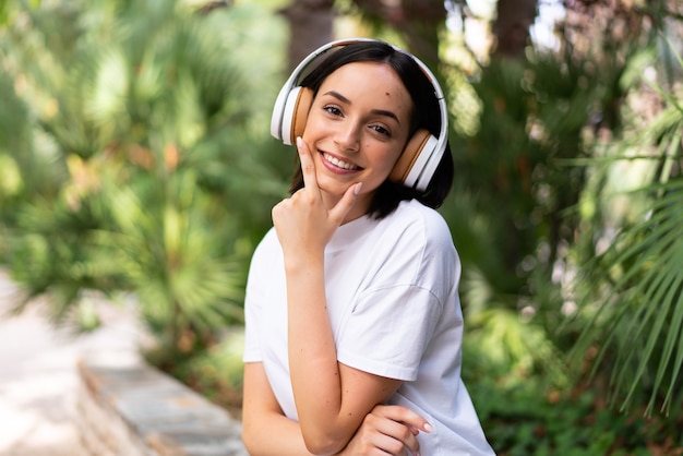 Young caucasian woman with headphones at outdoors smiling