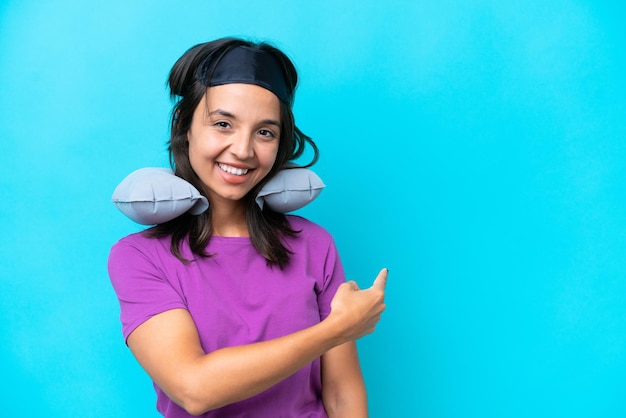 Young caucasian woman with Inflatable Travel Pillow isolated on blue background pointing back