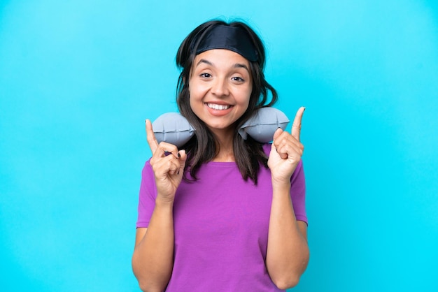 Young caucasian woman with Inflatable Travel Pillow isolated on blue background pointing up a great idea