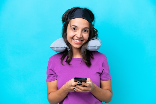 Young caucasian woman with Inflatable Travel Pillow isolated on blue background sending a message with the mobile