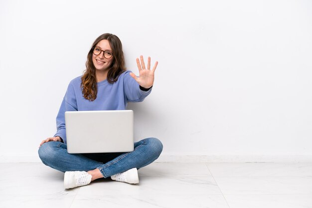 Young caucasian woman with a laptop sitting on the floor isolated on white background counting five with fingers