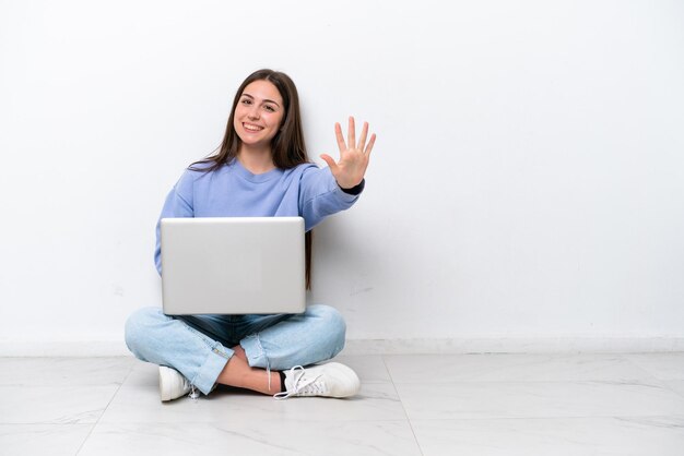 Young caucasian woman with laptop sitting on the floor isolated on white background counting five with fingers