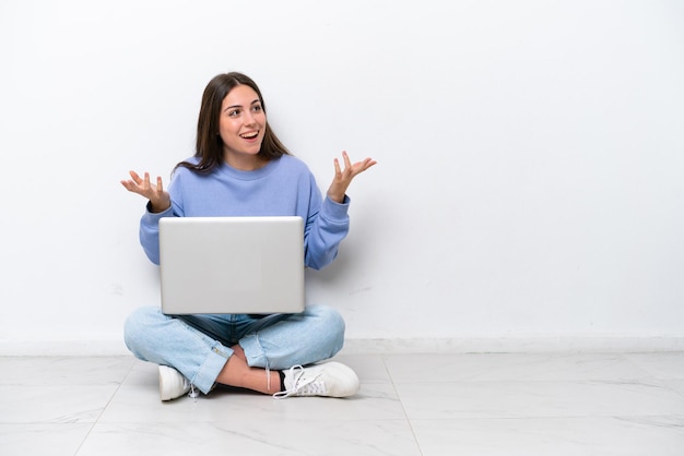 Young caucasian woman with laptop sitting on the floor isolated on white background with surprise facial expression