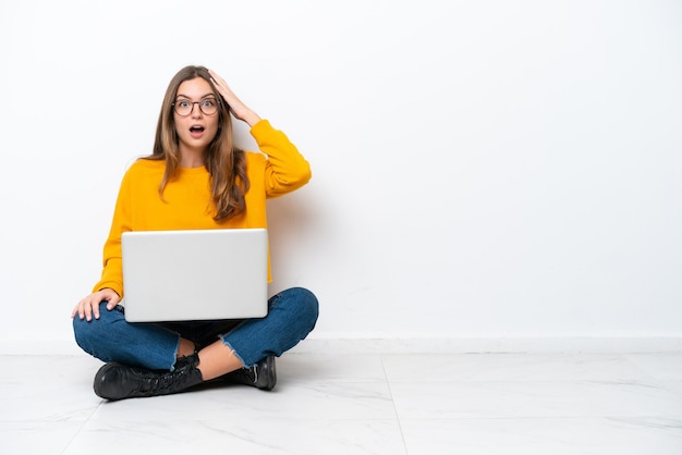 Young caucasian woman with a laptop sitting on the floor isolated on white background with surprise and shocked facial expression