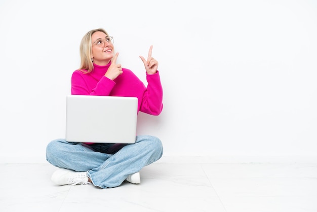 Young caucasian woman with laptop sitting on the floor pointing with the index finger a great idea