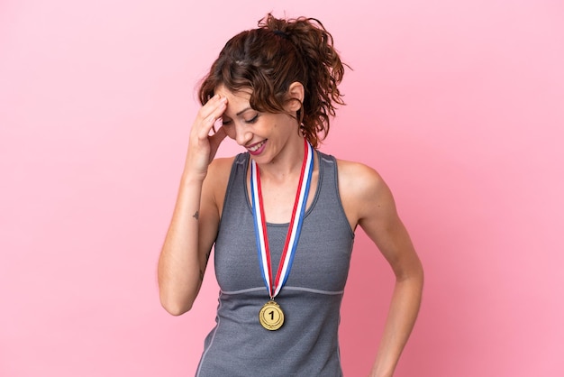 Young caucasian woman with medals isolated on pink background laughing